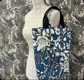 Blaue Tasche mit weißen Blumen und dunklen Henkeln